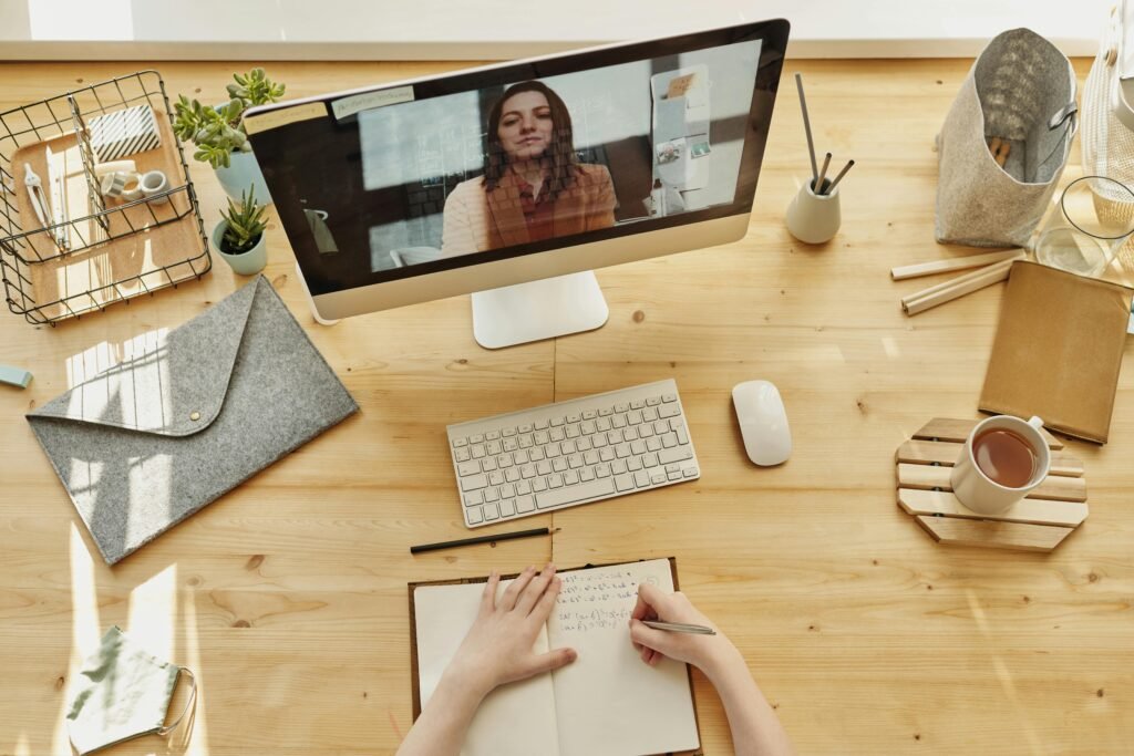 Person taking notes during a video call at a neatly organized home desk, showing remote work lifestyle.